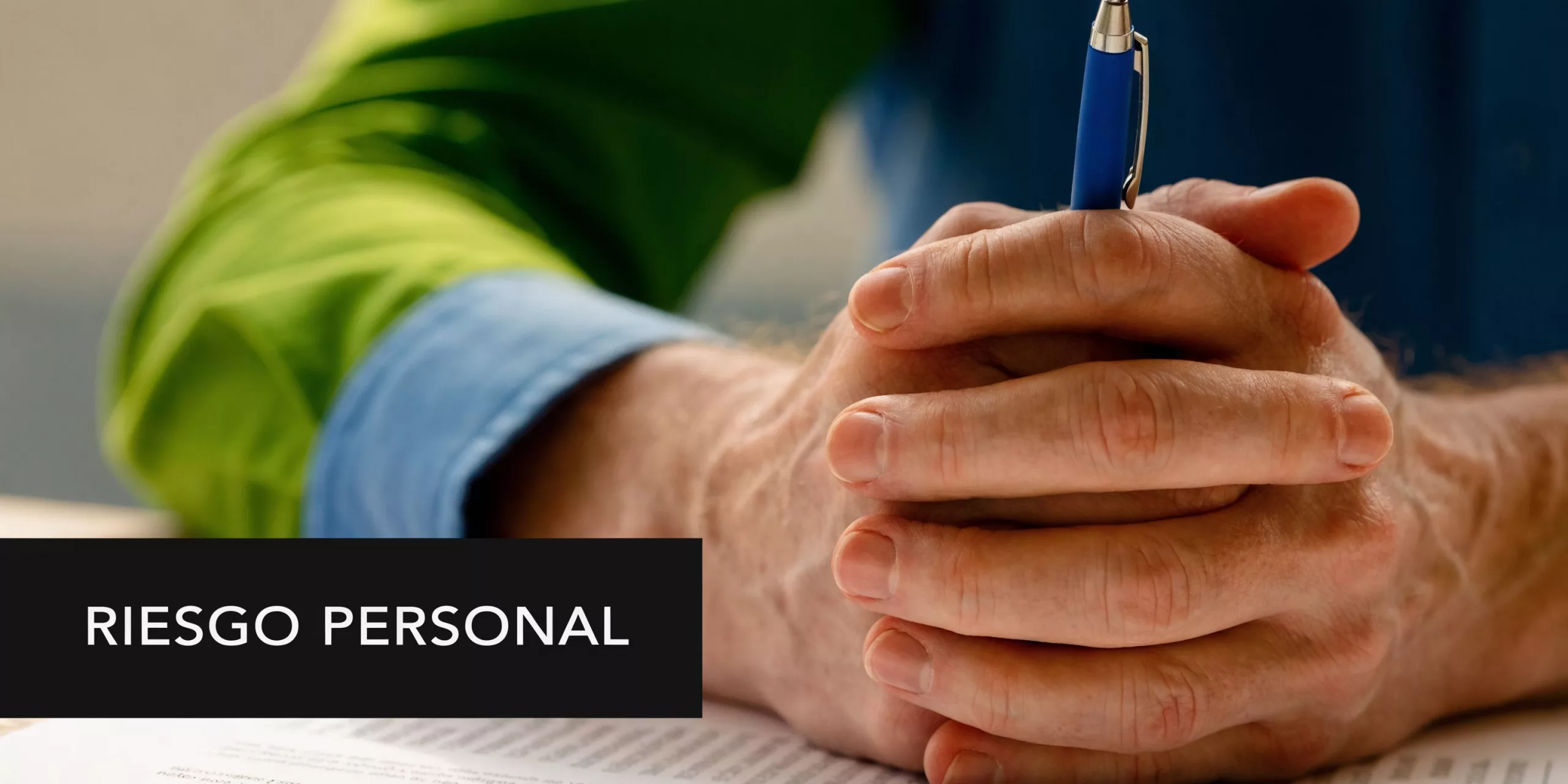 Persona con las manos entrelazadas sobre documentos legales junto a un bolígrafo, representando el concepto de riesgo personal.